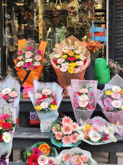 A variety of fresh flower bouquets displayed outside the Central Parade New Addington flowers shop, arranged on a wooden table in front of the shop window. The arrangements include pink, white, yellow