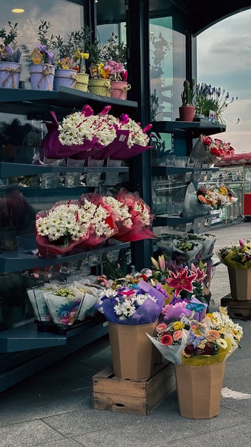 A display of fresh flower bouquets arranged on dark metal shelves and in brown paper and cardboard wrapping outside near the Near New Addington Tram Stop. The flowers include white daisies, pink lilie