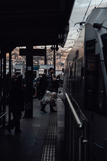 No flowers are visible in this image of a train station platform near New Addington Tram Stop. The scene shows passengers waiting, some carrying bags, with a modern train on the right side and overhea